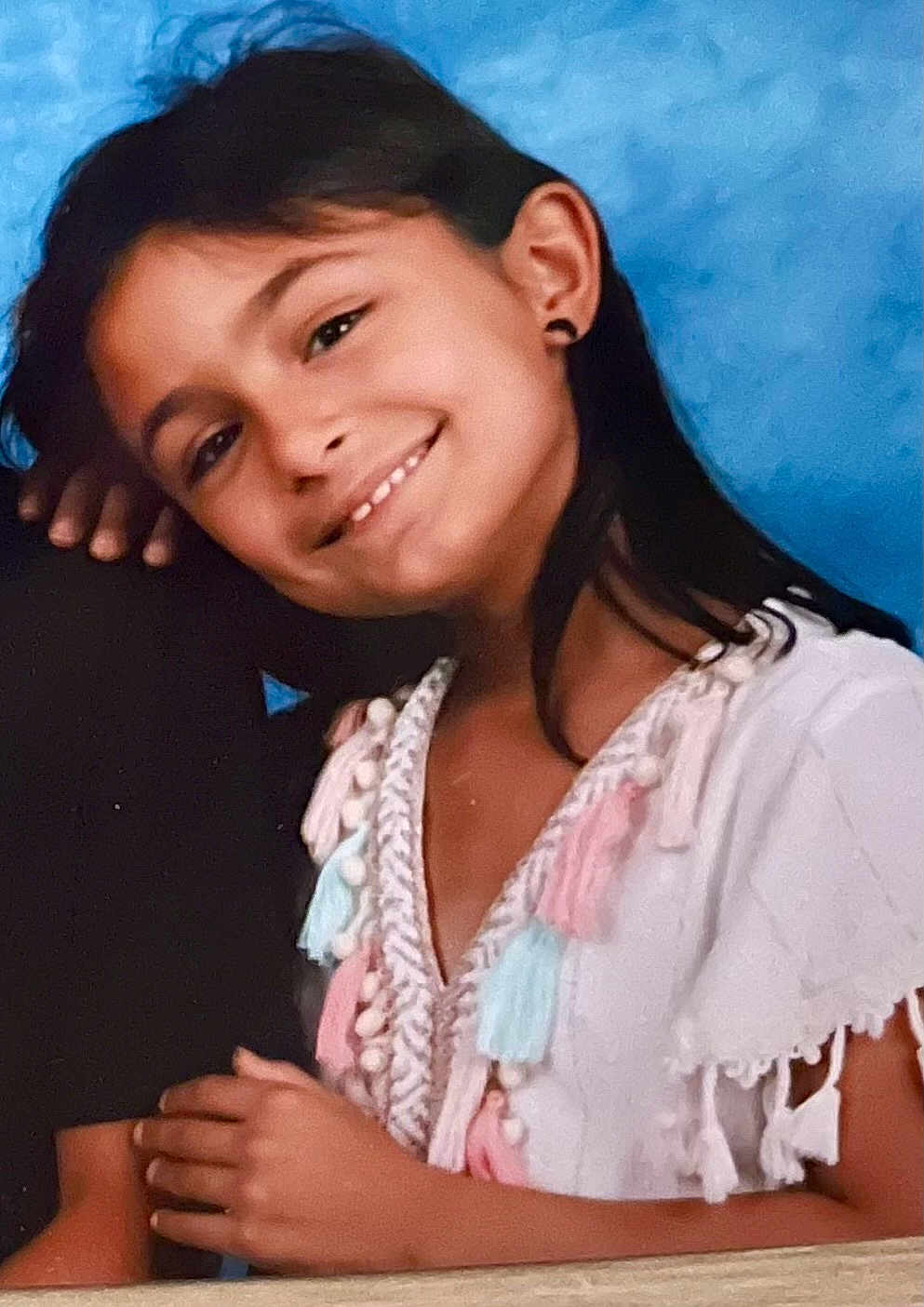Lana participe au concours pour gagner de l'argent avec cette photo : child, girl, smile, portrait, long_hair, earrings, white_top, tassels, pastel_colors, hand, blue_background, happy, casual, young, cute, face, clothing, person, indoor, friendly
