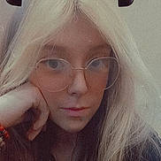 Breanna joined the competition — help win amazing prizes! person, face, close_up, glasses, blonde_hair, long_hair, portrait, selfie, hand_on_face, neutral_expression, vintage_filter, grainy, indoors, young_person, eyewear, nose, lips, bracelet, candid, hair