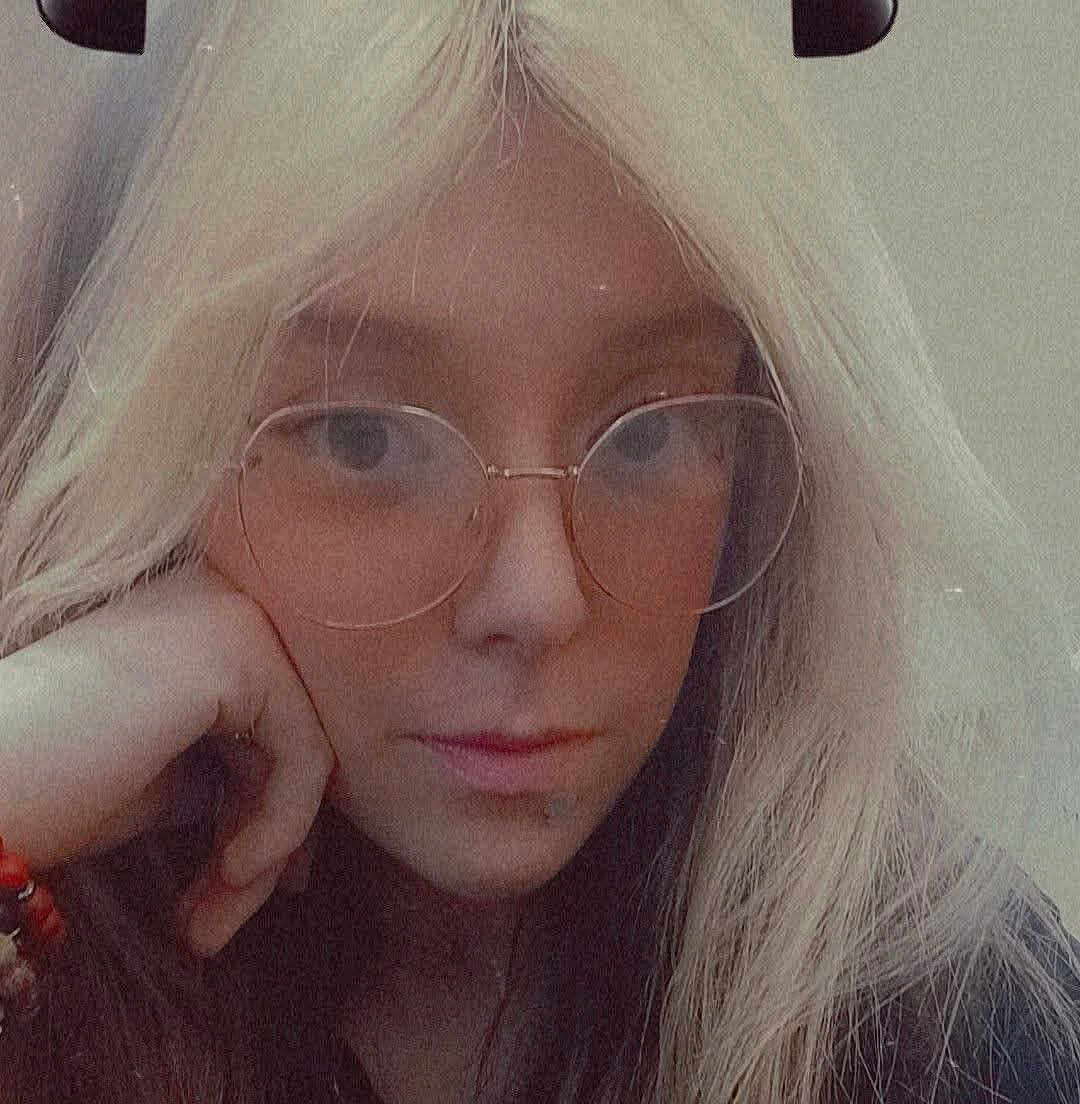 Breanna joined the competition — help win amazing prizes! person, face, close_up, glasses, blonde_hair, long_hair, portrait, selfie, hand_on_face, neutral_expression, vintage_filter, grainy, indoors, young_person, eyewear, nose, lips, bracelet, candid, hair