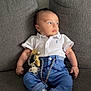 baby, child, polo_shirt, blue_pants, pacifier, couch, grey_couch, infant, clothing, socks, baby_toy, relaxed, indoor, portrait, seated, cute, small_hands, looking_away, home, comfort