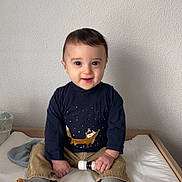Emilio a rejoint le concours — aidez-le/la à gagner de superbes lots ! baby, bed, bottle, casual_clothing, child, curious, cute, fox_design, indoor, long_sleeve_shirt, neutral_background, pants, person, sitting, smiling, socks, toddler, wall, white_bed_sheet, young_child