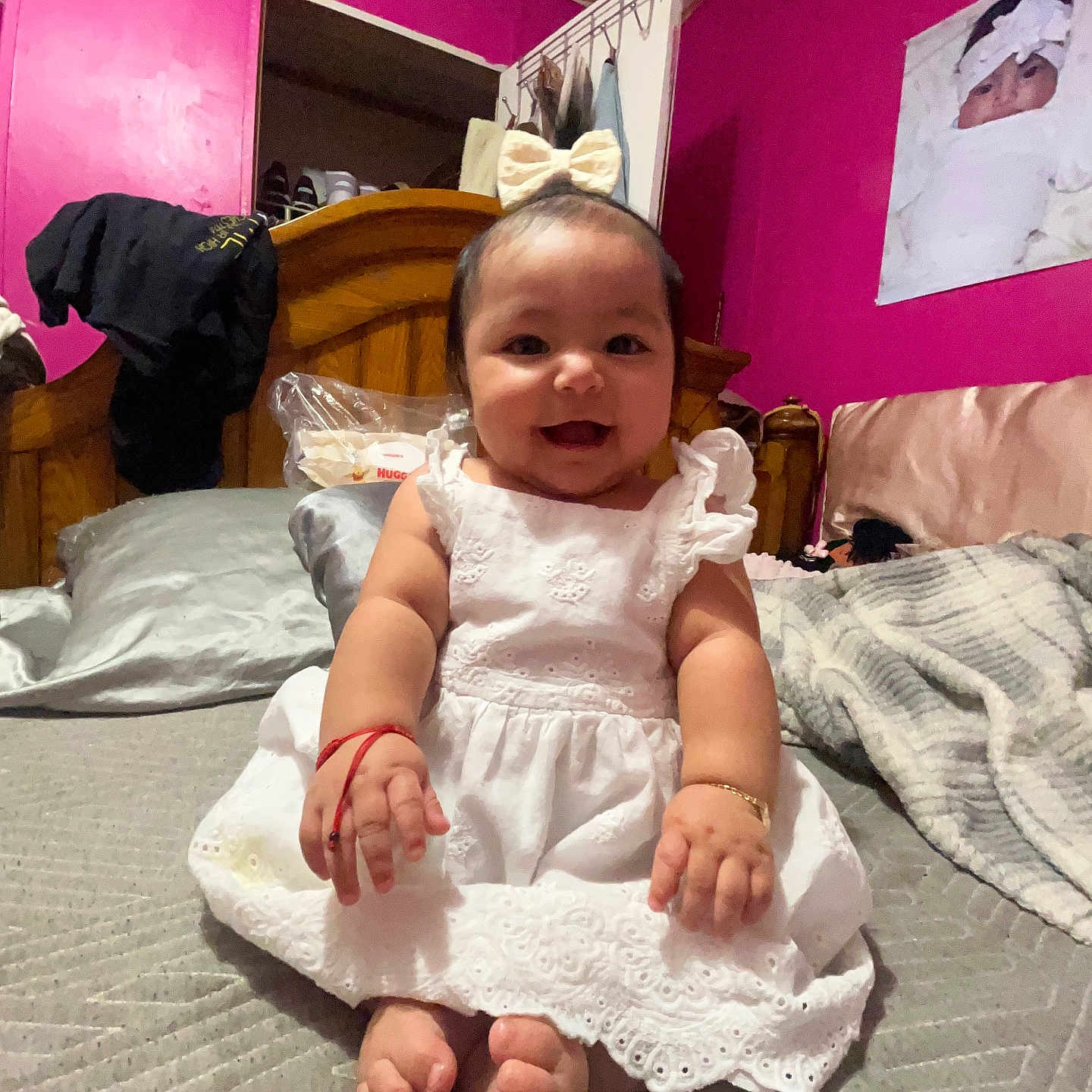 Marilu is registered to the contest to win money with this photo: baby, bed, blanket, bow, bracelet, child, cute, dress, fabric, feet, happy, indoors, infant, person, pink_wall, portrait, room, smiling, white_dress, wooden_headboard