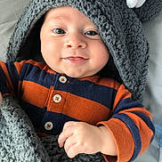 Woody is registered to the contest to win money with this photo: baby, blanket, child, cozy, cute, face, hand, happy, hood, indoors, infant, knitted, navy, onesie, orange, portrait, smiling, soft, striped, warm