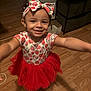 arms_outstretched, child, clothing, cute, dress, fashion, flooring, girl, hair_accessory, happy, headband, indoor, person, playful, portrait, red_tutu, smiling, strawberry_pattern, toddler, wooden_floor