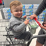 Charles joined the competition — help win amazing prizes! toddler, child, shopping_cart, smiling, supermarket, bottled_water, adult_hand, clothing, face, person, store, product_display, floor, shorts, gray_sweater, plastic_cup, grocery_shopping, happy, indoor, retail