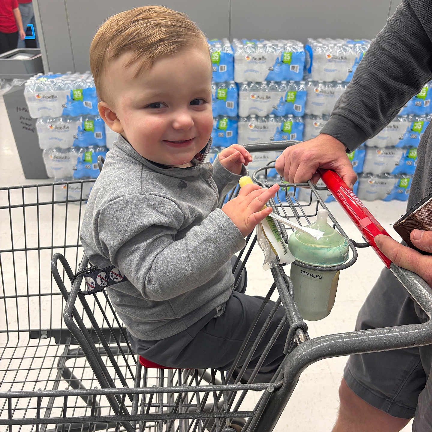 Charles joined the competition — help win amazing prizes! toddler, child, shopping_cart, smiling, supermarket, bottled_water, adult_hand, clothing, face, person, store, product_display, floor, shorts, gray_sweater, plastic_cup, grocery_shopping, happy, indoor, retail