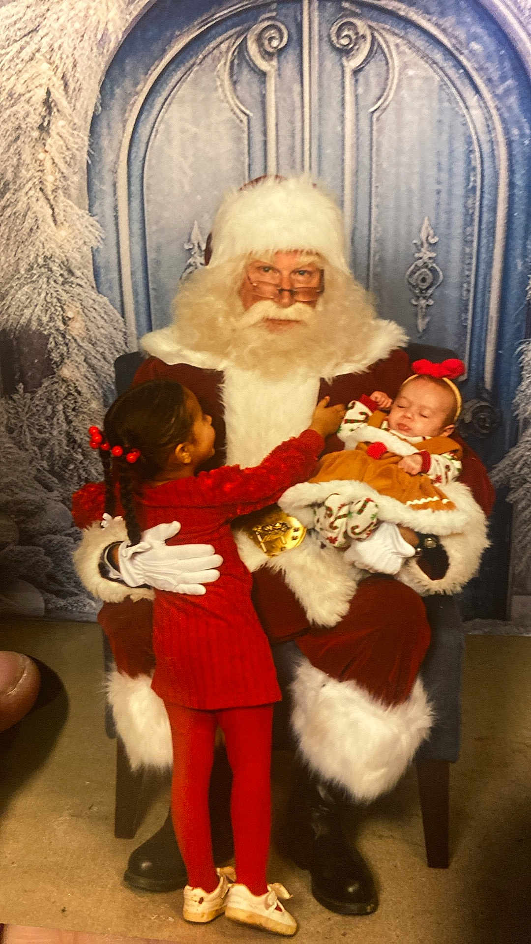 Nyla joined the competition — help win amazing prizes! santa_claus, child, baby, red_dress, holiday_clothing, christmas, winter_backdrop, glasses, beard, chair, tights, shoes, headband, indoor, portrait, festive, smiling, holding, seated, family