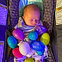 baby, sleeping, car_seat, plastic_eggs, easter_eggs, colorful, infant, clothing, blanket, patterned_pajamas, seat_belt, mesh_pocket, warning_labels, indoor, close_up, peaceful, child, toy, resting, cute