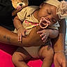 baby, infant, sleeping, pacifier, headband, bow, teddy_bear, stuffed_animal, onesie, baby_clothing, portrait, close_up, being_held, adult_arms, caregiver, indoors, cozy, pink_blanket, family, tender_moment
