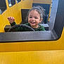 child, toddler, smiling, playground, steering_wheel, yellow, green_clothing, indoor, play_structure, happy, curly_hair, seat, window, hand_raised, face, person, fun, play, young, toy