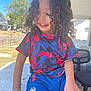 child, curly_hair, spiderman, tshirt, shorts, outdoor, daylight, smile, person, porch, chair, stop_sign, house, fence, grass, blue_sky, hand, casual_clothing, happy, seated