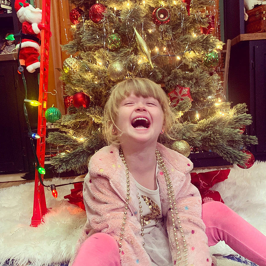 Cora joined the competition — help win amazing prizes! beauty, christmas, christmas_decoration, christmas_ornament, christmas_tree, event, facial_expression, fun, happy, holiday, holiday_ornament, human_body, ornament, person, photograph, smile, snapshot, standing, toddler, white