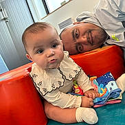 Manoune participe au concours pour gagner de l'argent avec cette photo : adult, baby, bonding, book, child, closeup, clothing, colorful, curious, face, family, happy, indoor, padded_surface, person, playtime, sitting, smiling, sock, toy