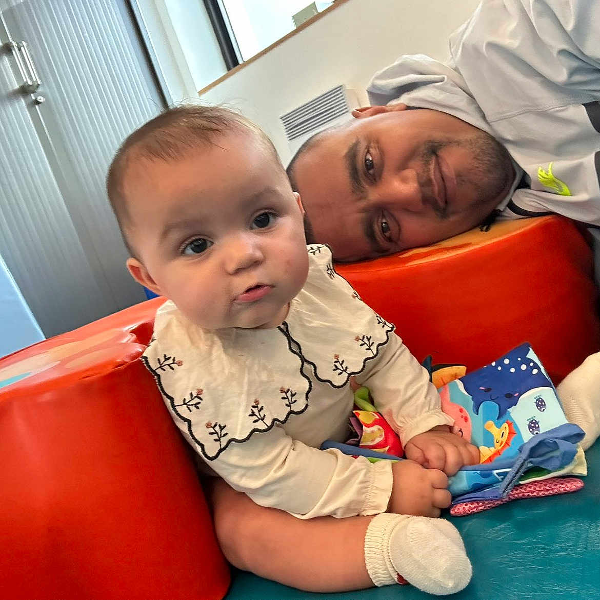 Manoune participe au concours pour gagner de l'argent avec cette photo : adult, baby, bonding, book, child, closeup, clothing, colorful, curious, face, family, happy, indoor, padded_surface, person, playtime, sitting, smiling, sock, toy