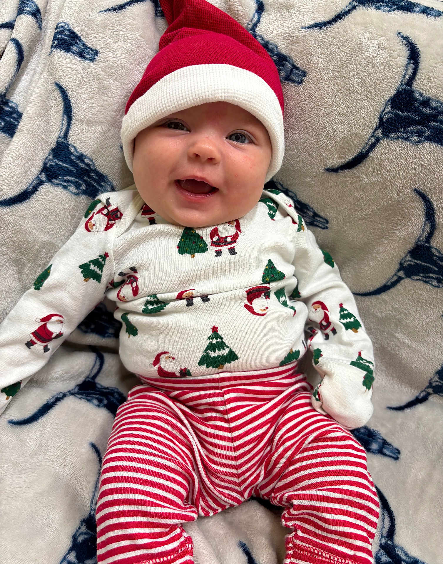 Adalynn is registered to the contest to win money with this photo: baby, infant, smiling, christmas, holiday, pajamas, hat, santa_hat, red, white, striped_pants, blanket, pattern, face, happy, cute, lying_down, cozy, festive, child