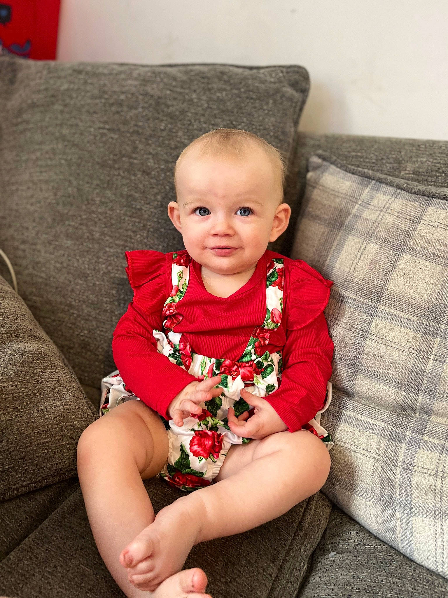 Gracie-mae is registered to the contest to win money with this photo: baby, baby_toddler_clothing, child, comfort, couch, dress, eye, face, happy, head, human_leg, joy, knee, lap, living_room, person, red, sitting, sleeve, smile