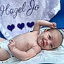 baby, infant, smile, face, skin, blanket, diaper, arm, head, blue_background, purple_hearts, text_on_blanket, lying_down, cute, newborn, person, soft_texture, happy, portrait, relaxed