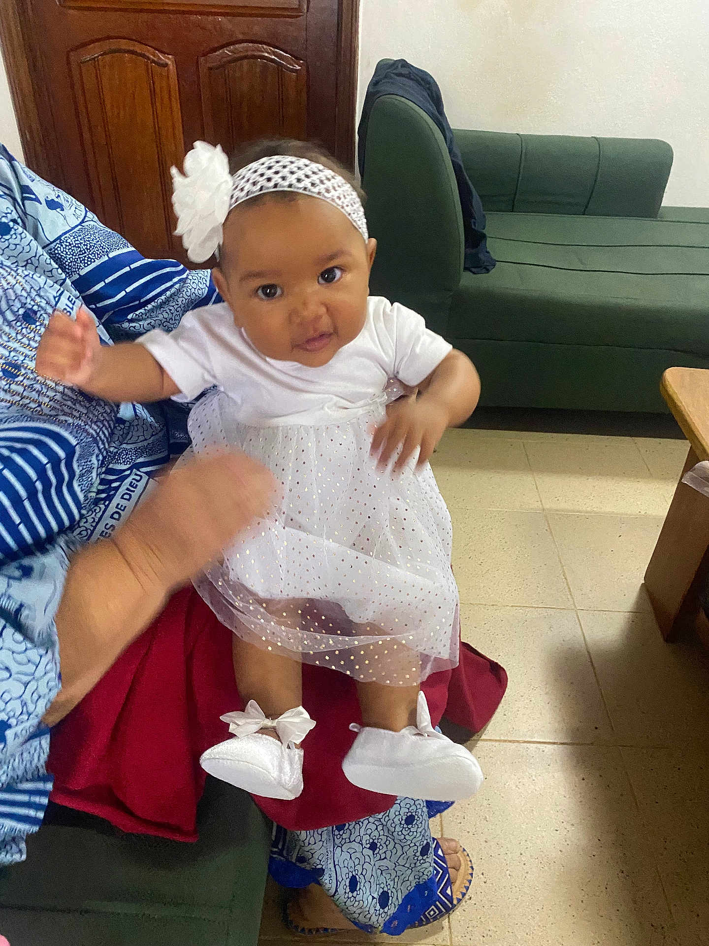 Athalia participe au concours pour gagner de l'argent avec cette photo : baby, child, white_dress, headband, flower, indoor, sofa, person, footwear, adult, hand, curious, patterned_clothing, floor, door, seated, couch, home, cute, infant