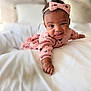 baby, infant, toddler, headband, bow, pink_clothing, bed, bedding, white_bed, blanket, smile, tongue_out, portrait, cute, crawling, hand, arm, face, skin, cozy