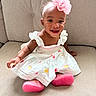 accessory, apparel, baby, child, couch, cute, dress, face, fashion, flower, happy, headband, indoors, infant, person, pink_shoes, portrait, seated, skin, smiling