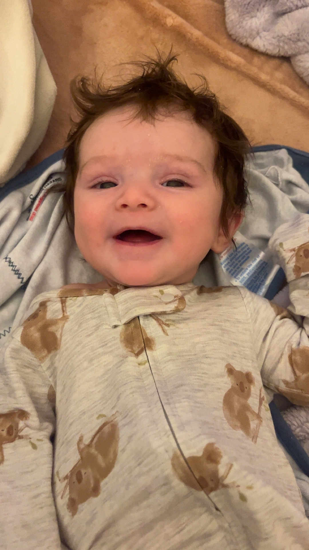Greyson is registered to the contest to win money with this photo: baby, smiling, face, child, pajamas, koala, sleepwear, blanket, soft, happy, cute, infant, toddler, clothing, lying_down, portrait, indoors, cozy, hair, expression