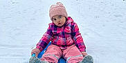 Leilani is registered to the contest to win money with this photo: toddler, child, snow, sled, winter_clothing, pink_hat, pink_gloves, boots, snow_pants, jacket, outdoor, play, pouty_face, snowy_ground, trees, house, cold_weather, fun, winter, blue_sled