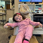 Leilani is registered to the contest to win money with this photo: child, girl, smile, pink_clothing, pink_shoes, dental_chair, office, computer_monitors, desk, flooring, happy, hair_accessory, indoor, person, furniture, waiting_room, medical_office, relaxed, casual, healthcare