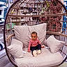 Dixie is registered to the contest to win money with this photo: child, baby, hanging_chair, cushion, seat, indoor, store, home_decor, person, furniture, shopping, retail, pillow, floor, carpet, clothing, footwear, cute, seated, expression