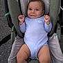 baby, infant, child, car_seat, onesie, smiling, face, blue_clothing, cushion, seat, safety, happy, person, cute, young, indoors, soft_texture, hand, legs, head