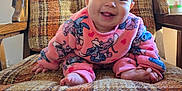 Kaori Delgado is registered to the contest to win money with this photo: baby, child, smiling, crawling, pink_clothing, cartoon_print, armchair, plaid_pattern, orange, brown, wooden_armrest, indoor, cozy, sunlight, happy, face, person, cute, foot, furniture