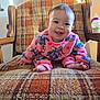 baby, child, smiling, crawling, pink_clothing, cartoon_print, armchair, plaid_pattern, orange, brown, wooden_armrest, indoor, cozy, sunlight, happy, face, person, cute, foot, furniture