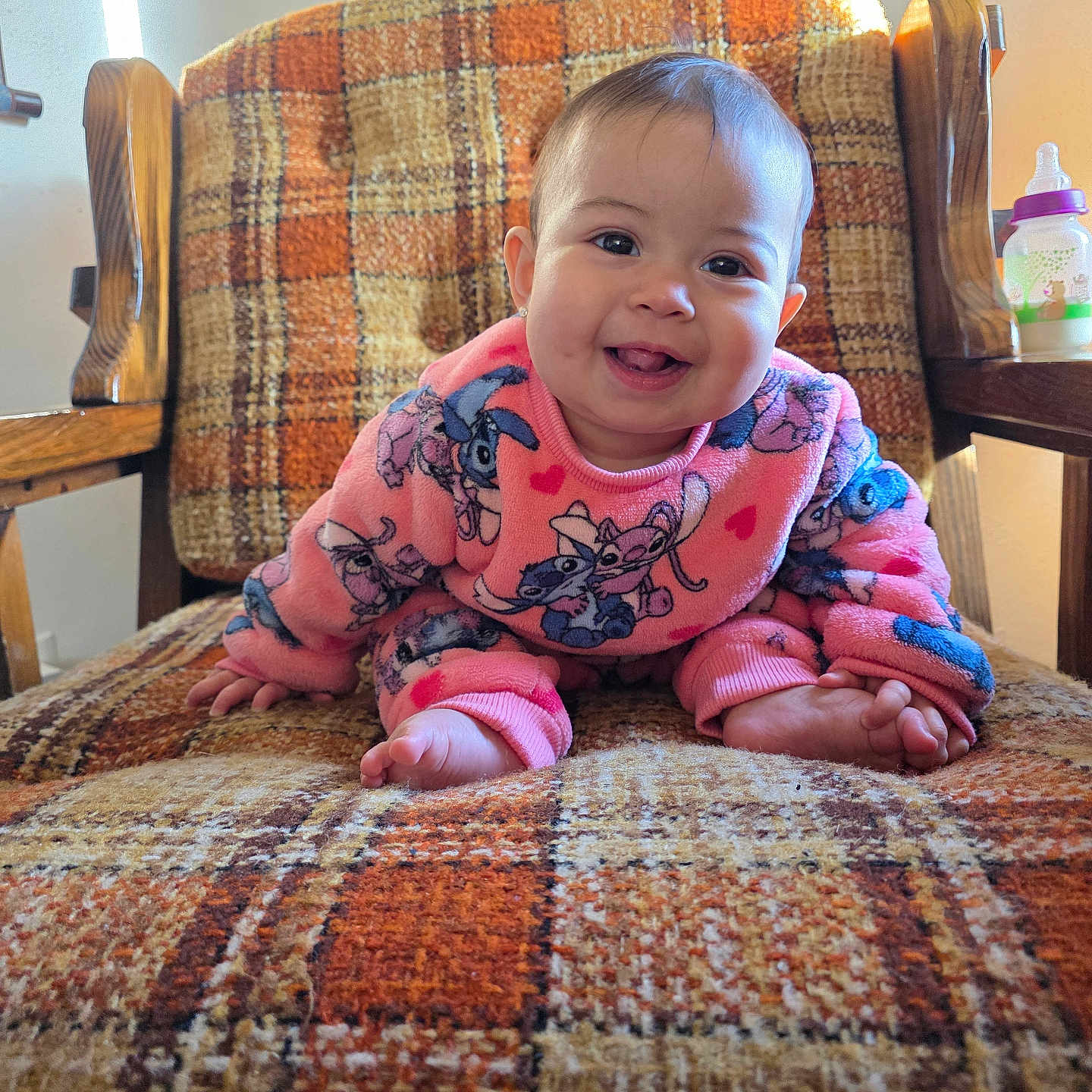 Kaori Delgado is registered to the contest to win money with this photo: armchair, baby, brown, cartoon_print, child, cozy, crawling, cute, face, foot, furniture, happy, indoor, orange, person, pink_clothing, plaid_pattern, smiling, sunlight, wooden_armrest