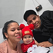 Kaori Delgado is registered to the contest to win money with this photo: baby, child, woman, man, family, indoor, smiling, hat, red_hat, dress, red_dress, white_dress, pom_poms, casual_clothing, portrait, happy, people, person, selfie, wall