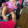 baby, infant, stroller, blanket, pink_clothing, foot, hand, wooden_floor, indoor, person, happy, smile, face, cozy, plush, cushion, child, casual, relaxed, home