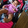baby, infant, stroller, blanket, pink_clothing, smile, indoor, wooden_floor, toy, foot, hand, face, child, person, cozy, relaxed, cute, home, cushion, casual