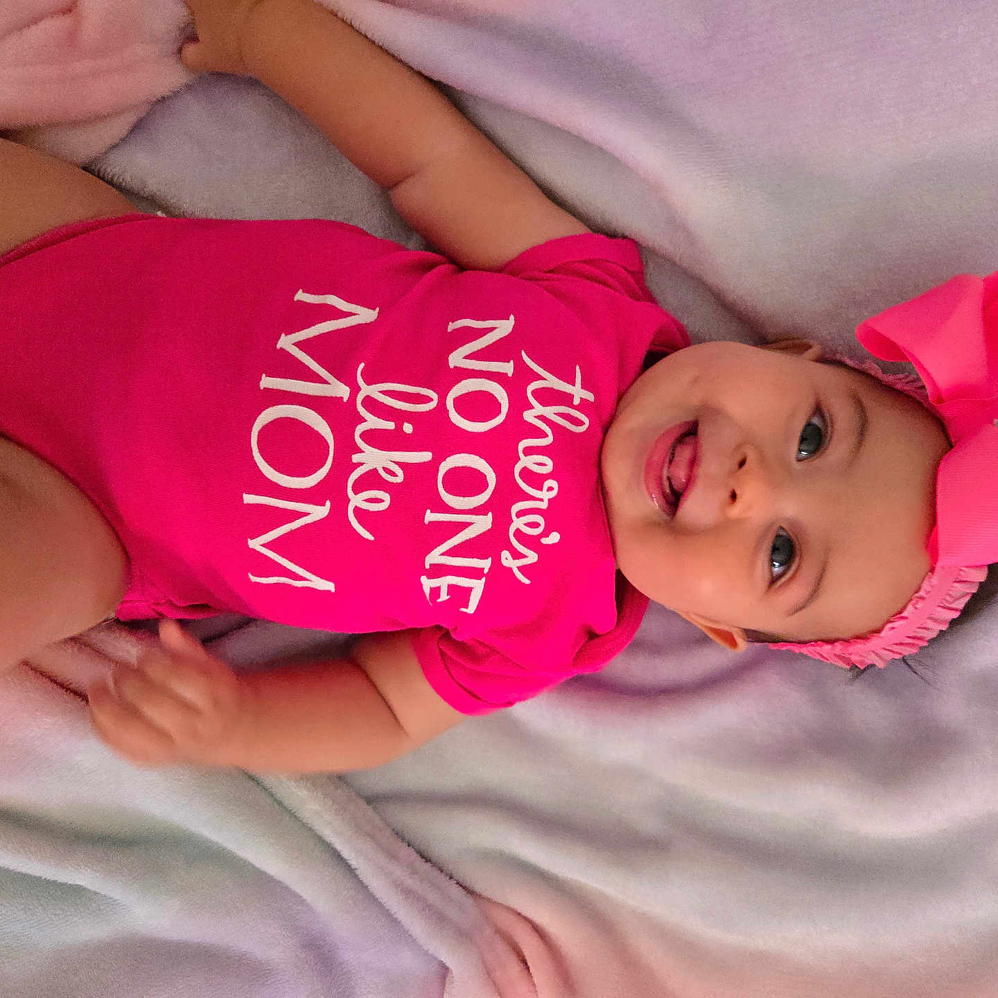 Kaori Hinata Delgado joined the competition — help win amazing prizes! baby, baby_girl, blanket, bow, child, clothing, cute, fabric, face, happy, headband, infant, lying_down, person, pink_onesie, playful, portrait, smiling, soft_texture, tongue_out