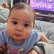 Kaori Hinata Delgado joined the competition — help win amazing prizes! baby, child, onesie, blue_clothing, face, eyes, blanket, indoor, television, cute, chubby_cheeks, hand, person, infant, portrait, bed, soft_texture, curious, young_child, cozy