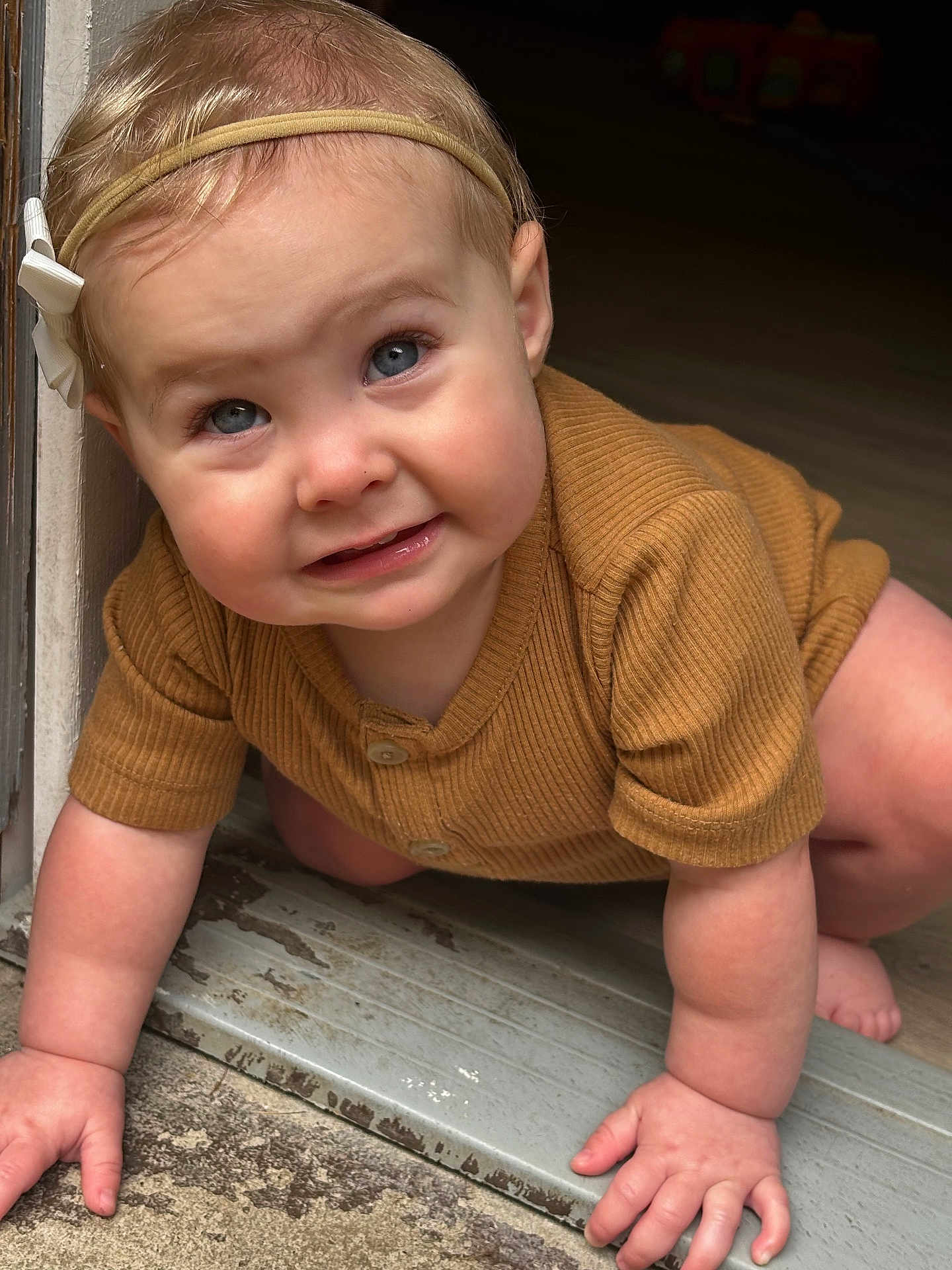 Journey is registered to the contest to win money with this photo: baby, child, crawling, headband, blue_eyes, brown_clothing, doorway, hands, floor, indoor, closeup, cute, infant, person, skin, smiling, young_child, portrait, happy, natural_light