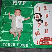 Nico joined the competition — help win amazing prizes! baby, infant, milestone_blanket, football, green, white, numbers, months, helmet, clothing, smile, happy, cute, child, blanket, laying_down, indoor, person, portrait, celebration