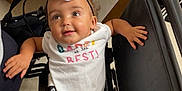 Brexley is registered to the contest to win money with this photo: baby, child, wheelchair, bow, onesie, hand, indoor, hospital, clinic, floor, seat, person, smile, curious, headband, foot, furniture, black, white, colorful_text