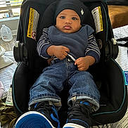 Alonzo is registered to the contest to win money with this photo: baby, child, car_seat, hat, blue_shoes, jeans, striped_shirt, indoor, window, blinds, bottle, blanket, bed, furniture, footwear, person, cute, clothing, sitting, portrait