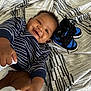 Alonzo is registered to the contest to win money with this photo: baby, smiling, striped_sweater, socks, diaper, nike_sneakers, blue, black, curly_hair, blanket, patterned_blanket, happy, infant, lying_down, foot, hand, close_up, indoor, child, cute