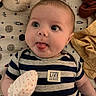 baby, infant, striped_shirt, mittens, face, tongue_out, teddy_bear, blanket, space_theme, pillow, cute, lying_down, soft_toys, child, playful, clothing, person, indoor, expression, newborn