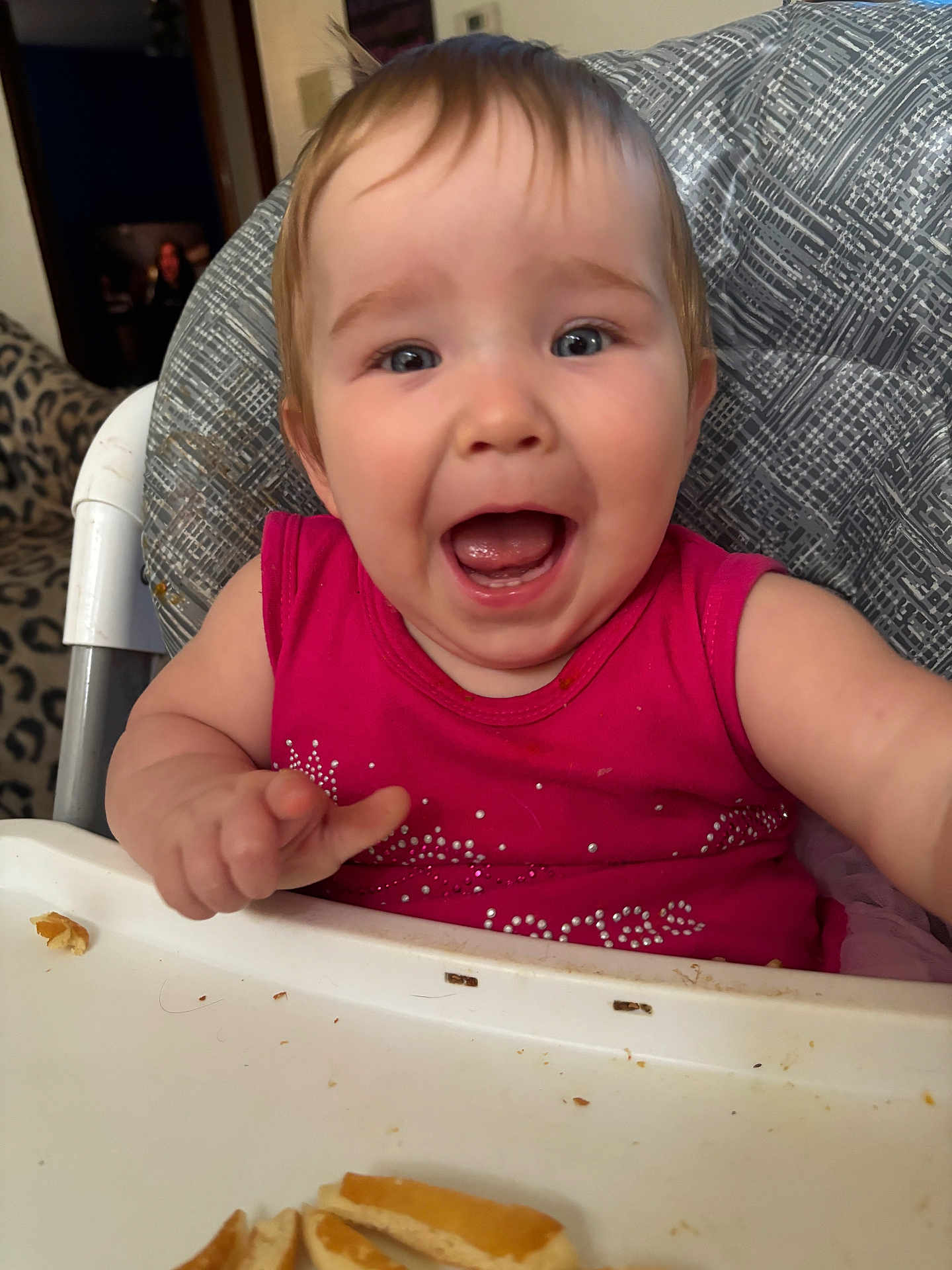 Aliyah is registered to the contest to win money with this photo: baby, child, high_chair, pink_shirt, happy, smiling, food, crumbs, face, mouth_open, indoor, person, seat, feeding, cute, expression, hair, table, furniture, living_room