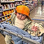 aisle, baby, blanket, child, clothing, cute, expression, face, floor, footwear, grocery_store, indoor, infant, orange_hat, person, retail, shopping, shopping_cart, socks, soft_toys