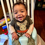 Noah is registered to the contest to win money with this photo: toddler, baby_seat, smiling, child, happy, clothing, camouflage, carhartt, indoor, furniture, wood_floor, toy, hair, face, person, sitting, cute, young_child, home, playful