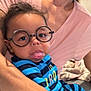 Noah joined the competition — help win amazing prizes! baby, glasses, tongue, striped_clothing, adult, smile, indoor, person, child, holding, face, cute, happy, seated, blue, black, pink_shirt, hand, portrait, expression