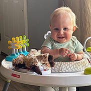 Ryder is registered to the contest to win money with this photo: baby, blonde_hair, blue_eyes, child, clothing, curtain, cute, door, flooring, furniture, happy, indoor, infant, person, playtime, plush_toy, seat, smiling, toy, walker