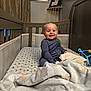 baby, crib, blanket, toy, child, indoor, smile, happy, furniture, bed, sleeping_area, person, face, clothing, curtain, wall, photography, infant, cute, room