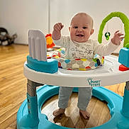 Ryder is registered to the contest to win money with this photo: baby, walker, smiling, indoor, child, toy, floor, happy, standing, colorful, feet, clothing, playtime, infant, face, person, bright, expression, wooden_floor, home